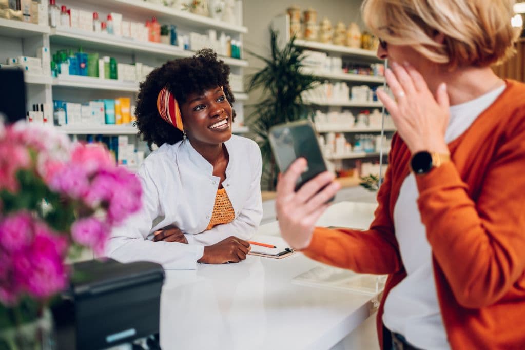 A pharmacist talking with a customer who is holding up her phone