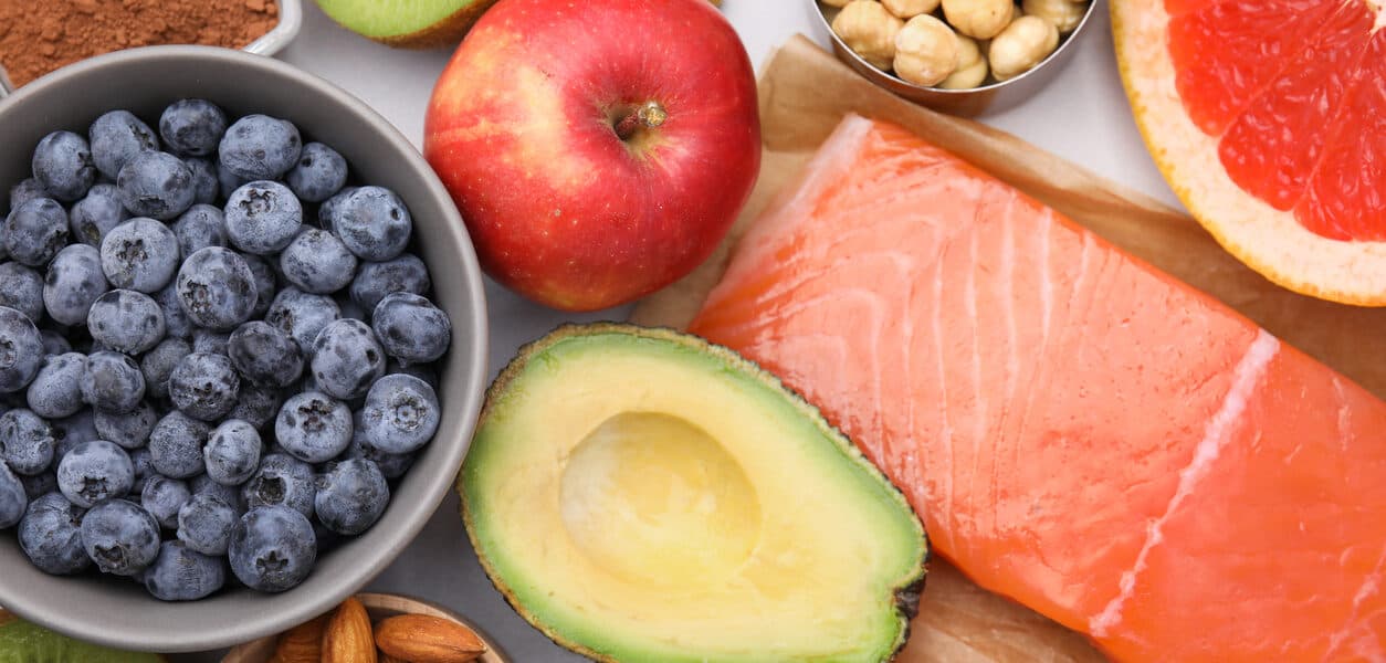 A variety of healthy foods: blueberries, an apple, avocado, salmon, grapefruit and nuts